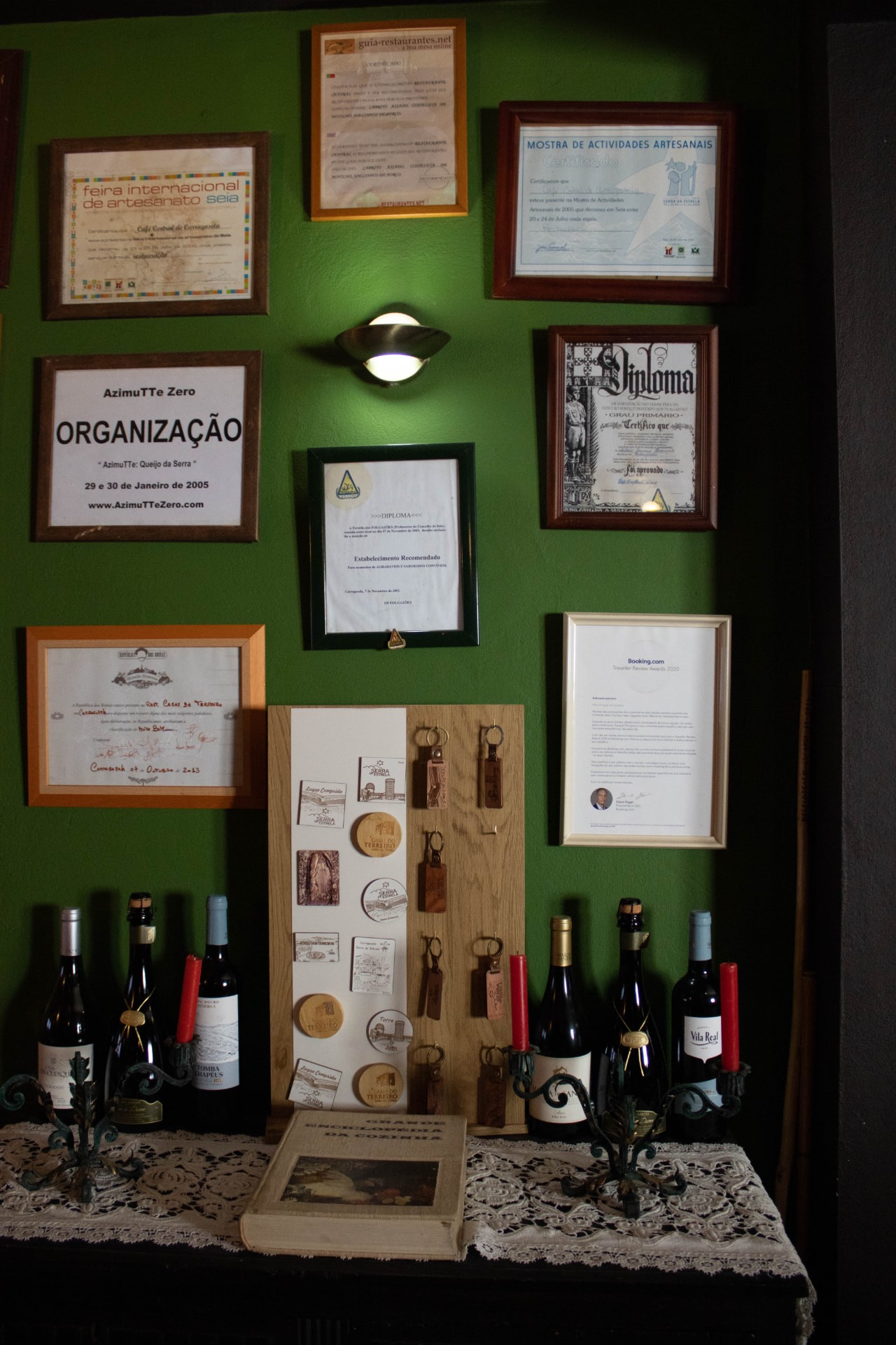 Entrada com garrafas de vinho, castiçais e diplomas emoldurados na parede verde