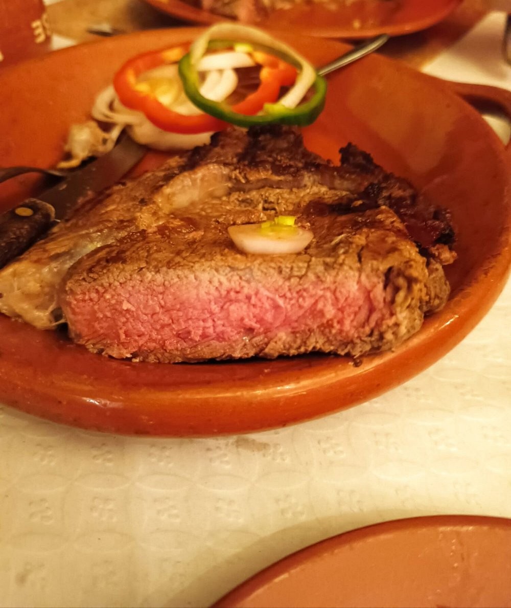 Posta de carne no ponto servida em prato de barro com pimentos e cebola